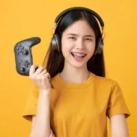 Asian woman in casual yellow t-shirt and playing video games using joysticks with headphones